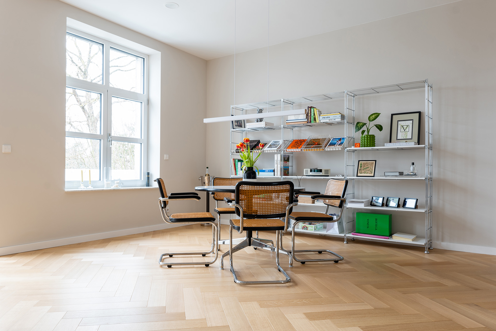 Referenz_Renovierung_Worms_Comfort_Tabis_XL_Eiche_Elegance_Natural_geölt Parkett in Fischgrat mit rundem Tisch sowie passenden Stühlen und einem Regal mit Bildern und Büchern
