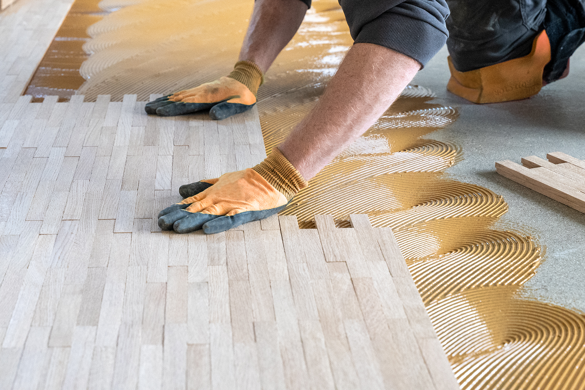 professionelle-verlegung-von-massivparkett Hände von Parkettlegern mit Handschuhen verlegt Massivparkett auf Boden mit Kleber.