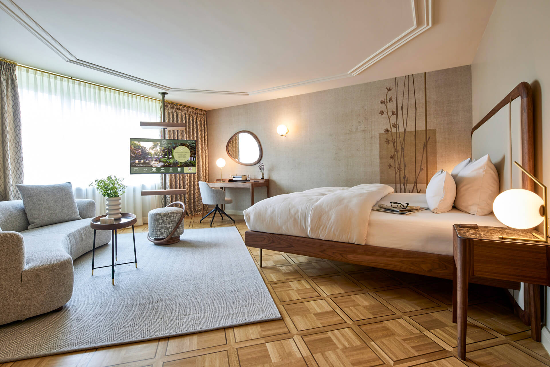 parkhotel-gütersloh-meisterparkett-eiche-ravenna-4 (1) Blick in ein Hotelzimmer im Parkhotel Gütersloh mit Meisterparkett Ravenna Eiche geölt, grauer Couch und großem Bett