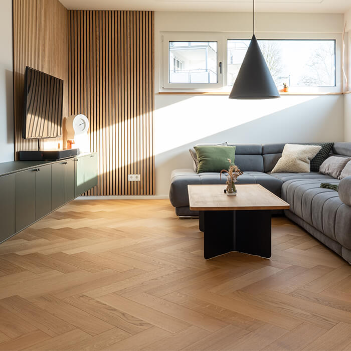 Modernes Wohnzimmer mit Comfort Tabis XL Fischgratparkett in Eiche Elegance geölt, grauem Ecksofa